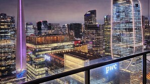 Bybillede med oplyste skyskrabere, herunder en markant bygning med 'PWC' skiltning.