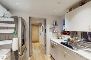 Eine moderne Küche mit einem Edelstahlkühlschrank, Holzboden, weißen Schränken und einer integrierten Spüle.