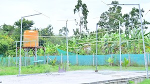 Uma plataforma de concreto com estrutura metálica, um reservatório de água e uma cerca verde com vegetação.