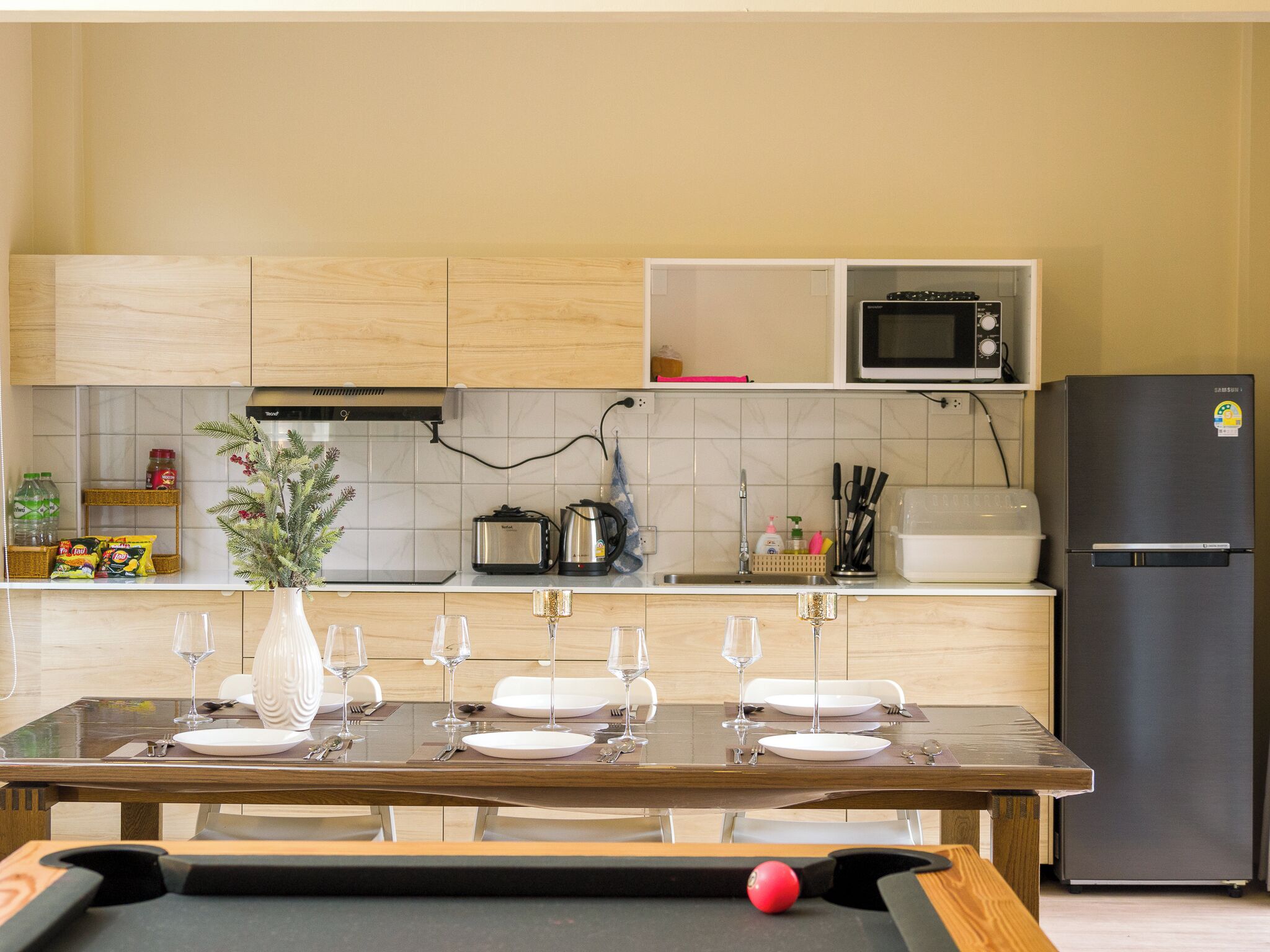 Een keuken met een eettafel voor zes personen, een magnetron, een koelkast en diverse keukenartikelen.