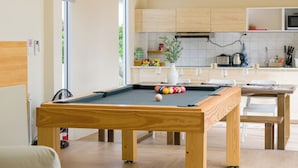Una mesa de billar en una habitación moderna con una cocina al fondo.