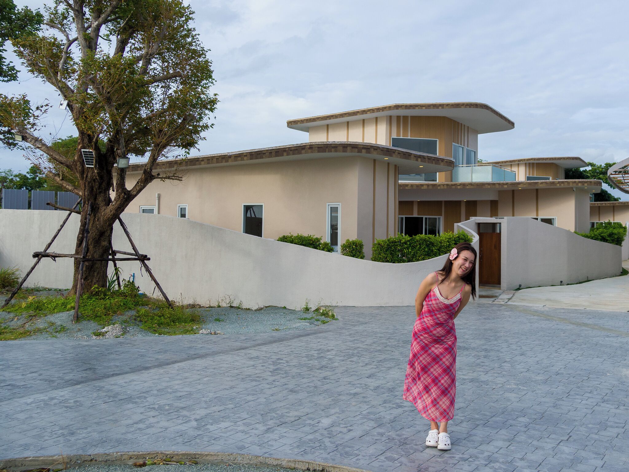 Una casa moderna con techo curvo, un árbol en primer plano y un camino pavimentado.