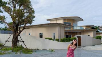 Una casa moderna con techo curvo, un árbol en primer plano y un camino pavimentado.