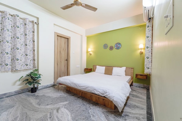 A bedroom with a bed, a ceiling fan, a potted plant, and decorative wall plates.