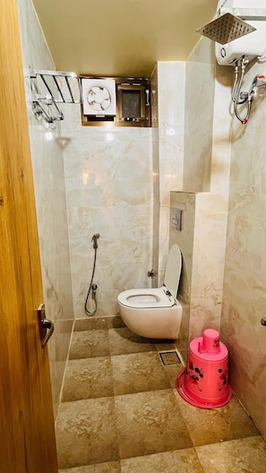 A bathroom with a toilet, shower, and a red bucket.