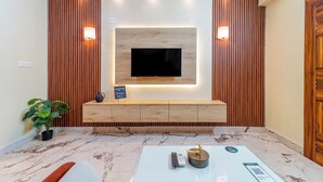 Een moderne woonkamer met een flatscreen televisie aan een houten wand, een console tafel, een potplant en een marmeren vloer.