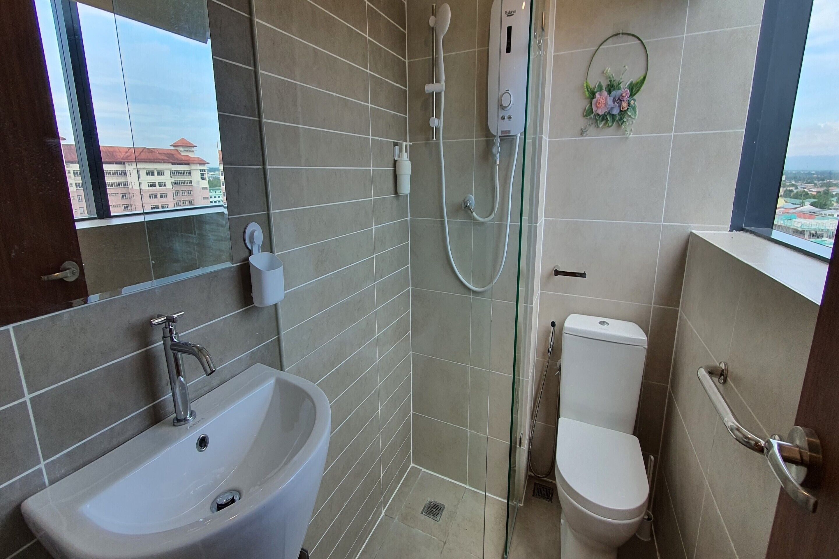 A bathroom with a sink, toilet, shower, and a window with a view of buildings.