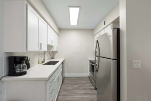 A compact kitchen with white cabinets, a stainless steel refrigerator, a coffee maker, and a small sink. - 2BR Modern Mesa Stay Near DT with Pools & Gym (Mesa)
