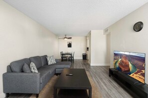 A living room with a sectional sofa, a coffee table, a flat-screen TV, a dining area with chairs, and a ceiling fan. - 2BR Modern Mesa Stay Near DT with Pools & Gym (Mesa)