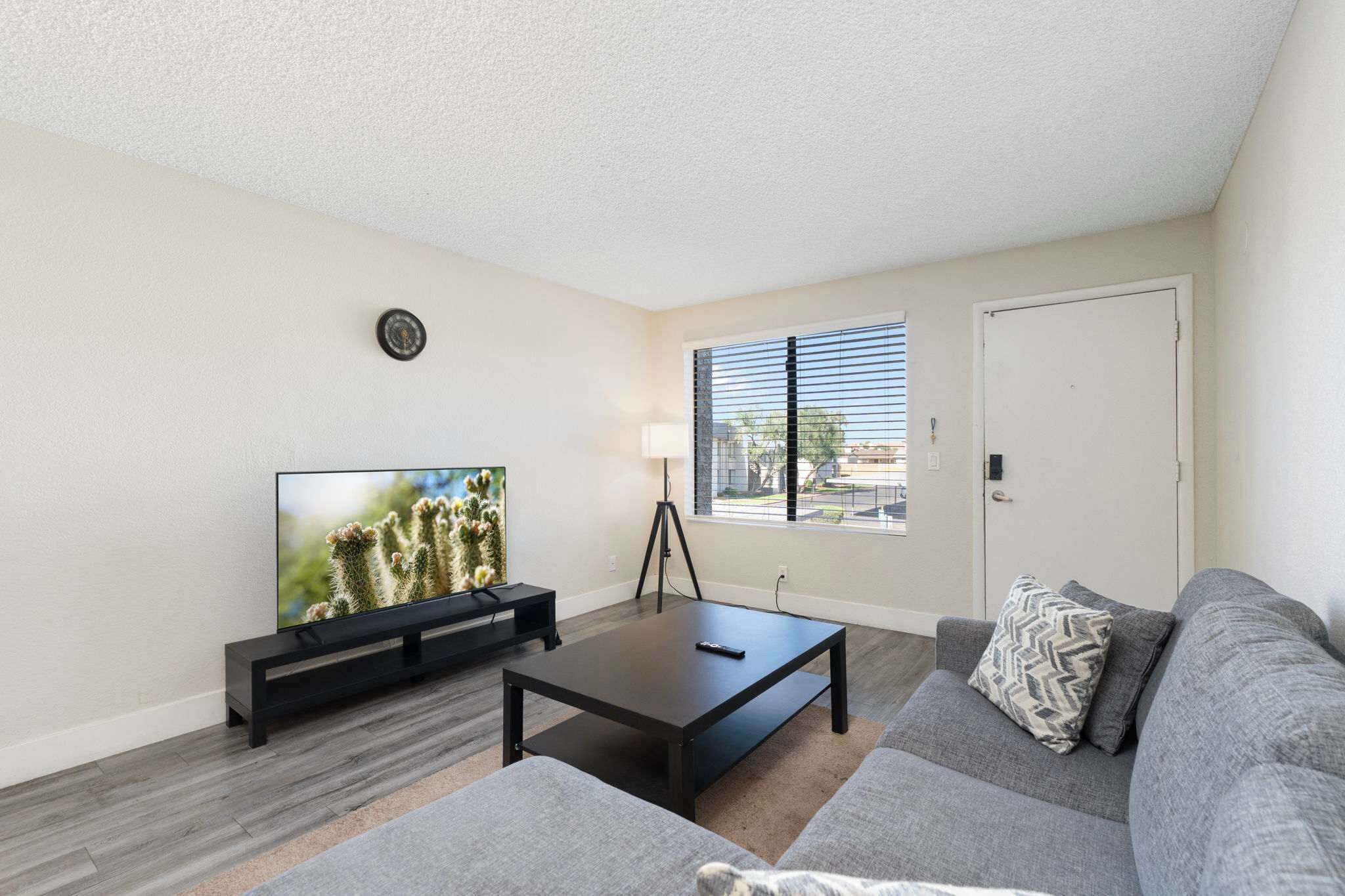 A living room with a flat-screen TV, a coffee table, a sofa, and a window with blinds.