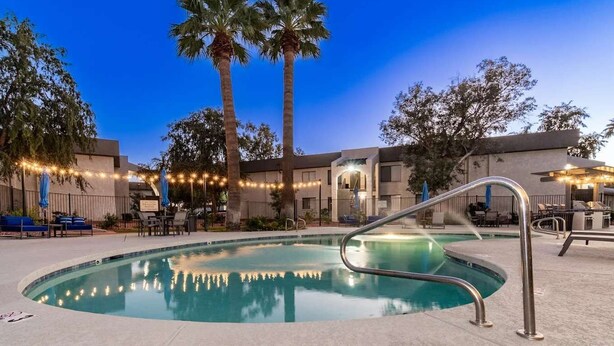 A swimming pool with a metal handrail, surrounded by palm trees and lounge chairs.