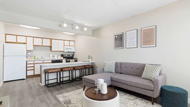 Un apartamento moderno con cocina, un sofá gris, una mesa de centro redonda y un reposapiés azul.