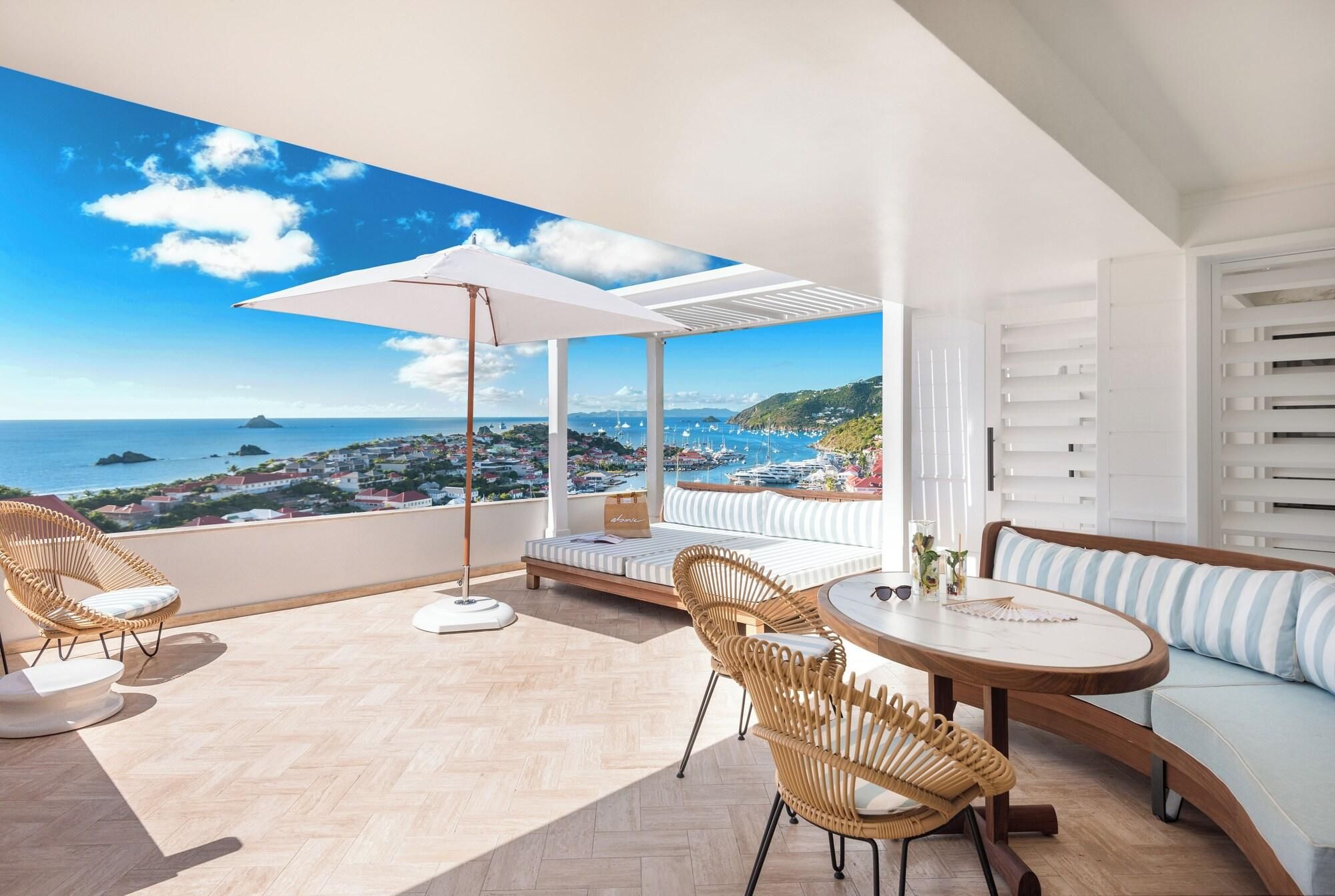 A balcony with wicker chairs, a round table, and a sofa with a view of the sea and town.