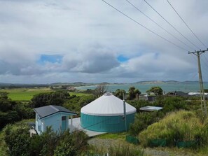 A large, round, white-roofed structure surrounded by greenery and houses, overlooking a coastal landscape.