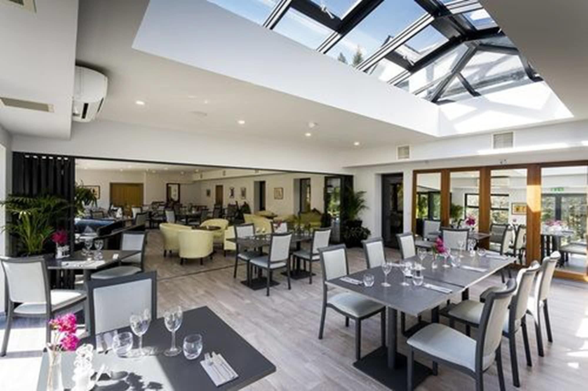 A spacious interior with a high ceiling and skylight, featuring multiple dining areas with tables and chairs.