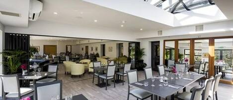 A spacious interior with a high ceiling and skylight, featuring multiple dining areas with tables and chairs.