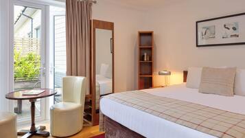 Una habitación de hotel con una cama, una silla, una mesita, una estantería y una ventana con cortinas.
