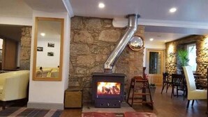 A room with a stone wall, a fireplace with a visible fire, a wooden table, and a chair. - The Brander Lodge Hotel And Bistro (Taynuilt)