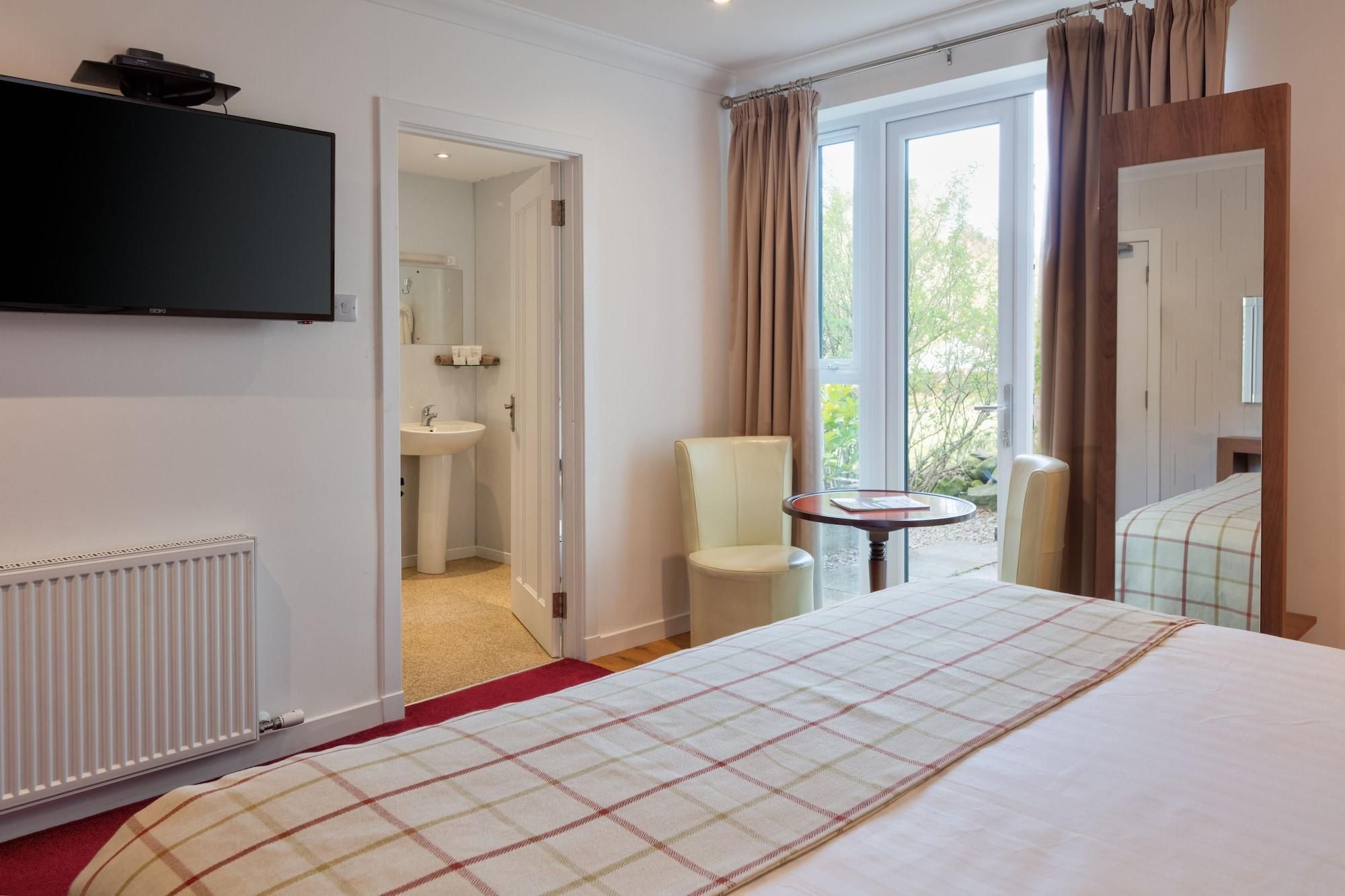 A hotel room with a bed, a TV, a bathroom, and a view of the outdoors.