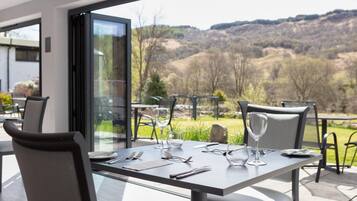 Una mesa de comedor con cubiertos y vasos, con vistas a un paisaje montañoso.