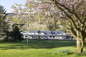 Un bâtiment doté d’un toit plat et de nombreuses fenêtres, entouré d’une pelouse bien entretenue et d’un grand arbre aux fleurs roses.