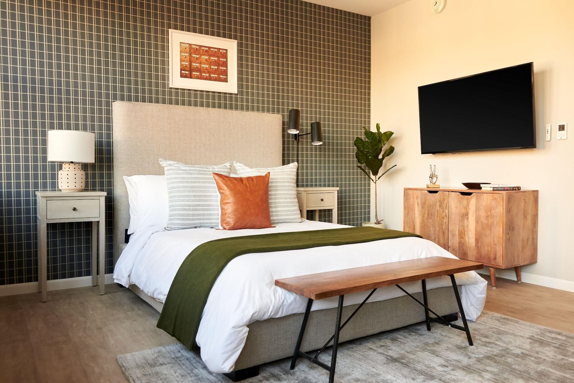 Ein modernes Schlafzimmer mit einem Bett, Nachttischen, einem Fernseher und einer hölzernen Sitzbank.