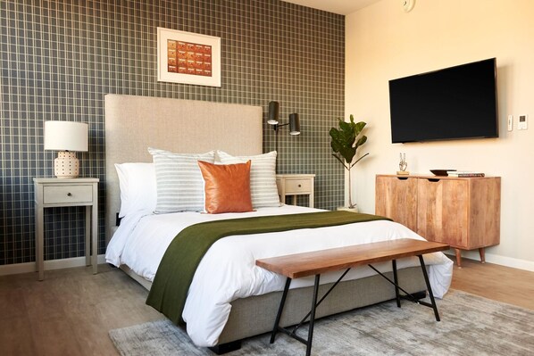 A modern bedroom with a bed, bedside tables, a TV, and a wooden bench.