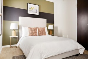 A hotel room with a bed, two bedside tables, a lamp on each table, a framed picture on the wall, and a door.