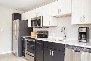 A modern kitchen with stainless steel appliances, white cabinetry, and a built-in dishwasher.