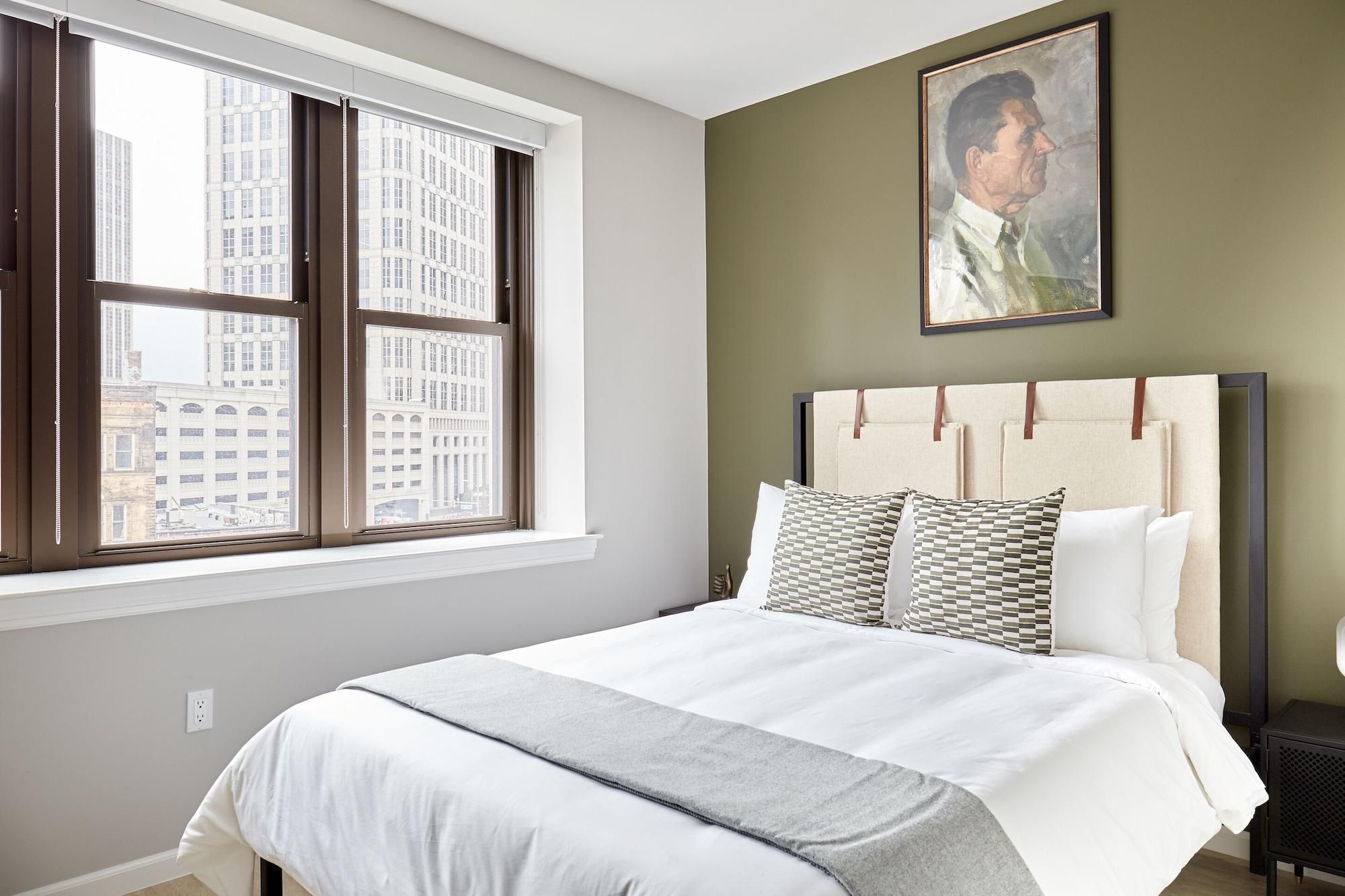 Een slaapkamer met een groot raam, een bed met hoofdeinde en een schilderij aan de muur.