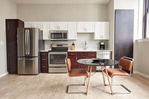 A compact kitchen with a refrigerator, microwave, stove, and a dining area with two chairs and a table. - Sonder The Randolph (Detroit)