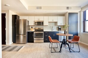 A modern kitchen with stainless steel appliances, a dining area with two chairs, and a window providing natural light. - Sonder The Randolph (Detroit)