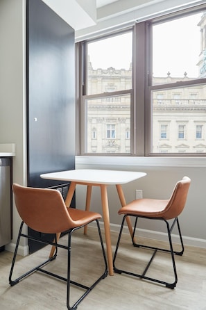 A room with two chairs and a table, large windows with a view of buildings, and a black wall. - Sonder The Randolph (Detroit)