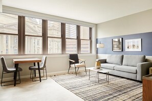 A modern living room with a large window, a sofa, a coffee table, and two chairs. - Sonder The Randolph (Detroit)