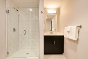A bathroom with a glass-enclosed shower, a sink with a mirror, and a dark cabinet. - Sonder The Randolph (Detroit)