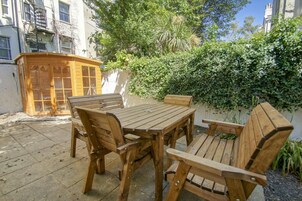 Un conjunto de mesa y sillas de madera al aire libre, con un edificio en el fondo.