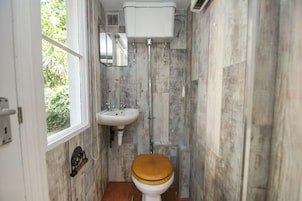 Un baño con inodoro de madera, lavamanos blanco y ventana.