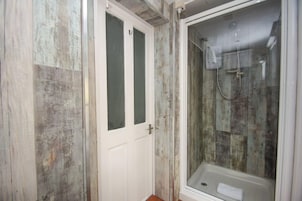 Un baño con ducha, una puerta y una ventana.