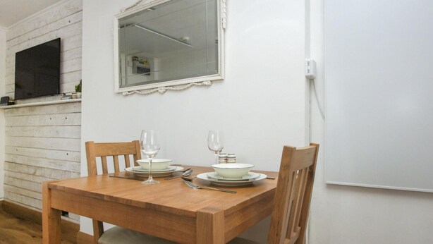 Een houten eettafel met stoelen, een spiegel erboven en een witte muur met een stopcontact.