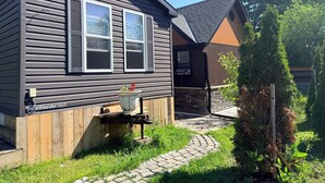 A house with a chimney, a window, a small outdoor seating area, and a wooden deck.