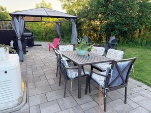 An outdoor patio with a table and chairs, a covered seating area, and a grill.