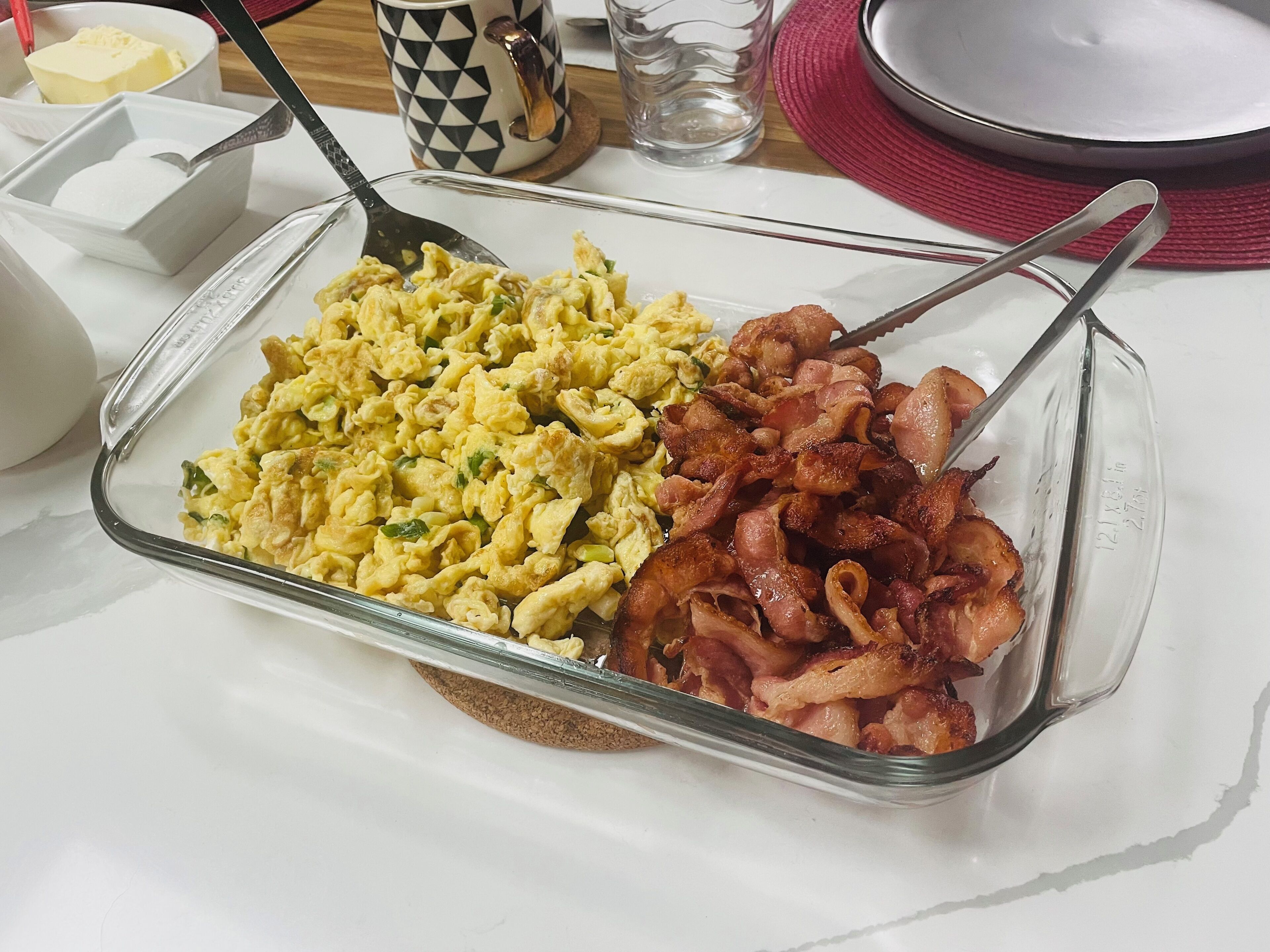Un plateau de petit-déjeuner avec des œufs brouillés, du bacon et du beurre, posé sur une table blanche.
