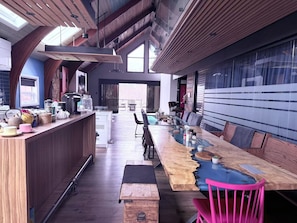 Une cuisine moderne dotĂ©e dâun grand Ăźlot central en bois, dâun coin repas avec une table en verre et dâune vue sur une piscine.