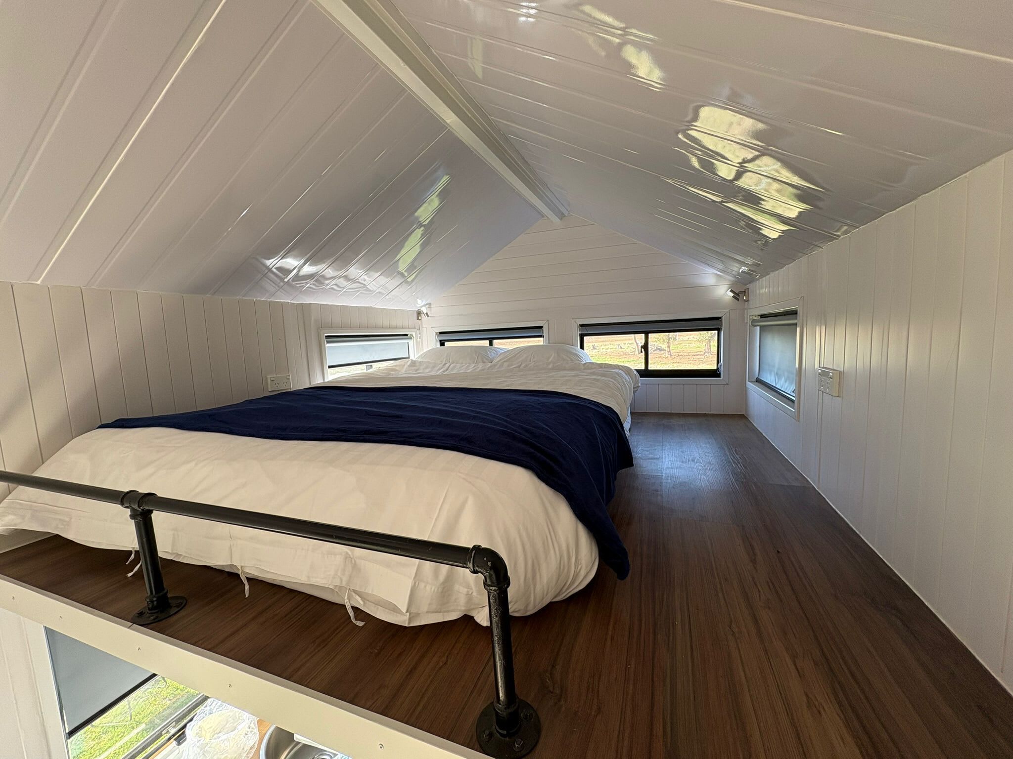 A bedroom with a bed, a window, and a view of the outdoors.. Loft Tiny House by Tiny Away