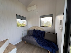 A small room with a bed, two windows, a ceiling fan, and a built-in air conditioning unit.