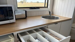 Una cocina con microondas, lavamanos y un organizador de cajones con utensilios.