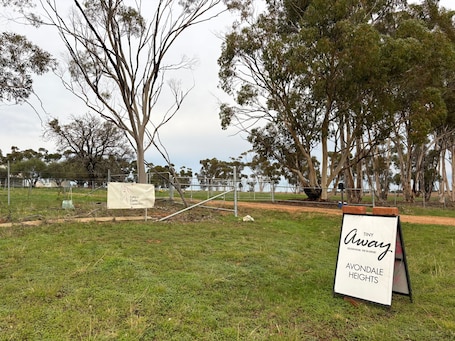 A signboard with 'Tiny Away' and 'Avondale Heights' text, a fenced area, and trees.. Loft Tiny House by Tiny Away