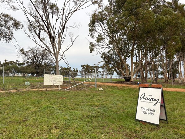 A signboard with 'Tiny Away' and 'Avondale Heights' text, a fenced area, and trees.