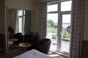 A hotel room with a balcony, a bed, two chairs, and a small table.