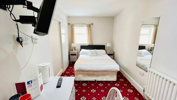 A hotel room with a bed, a desk with a computer, a chair, a TV mounted on the wall, and a window with curtains. - Chatsworth Hotel (Skegness)